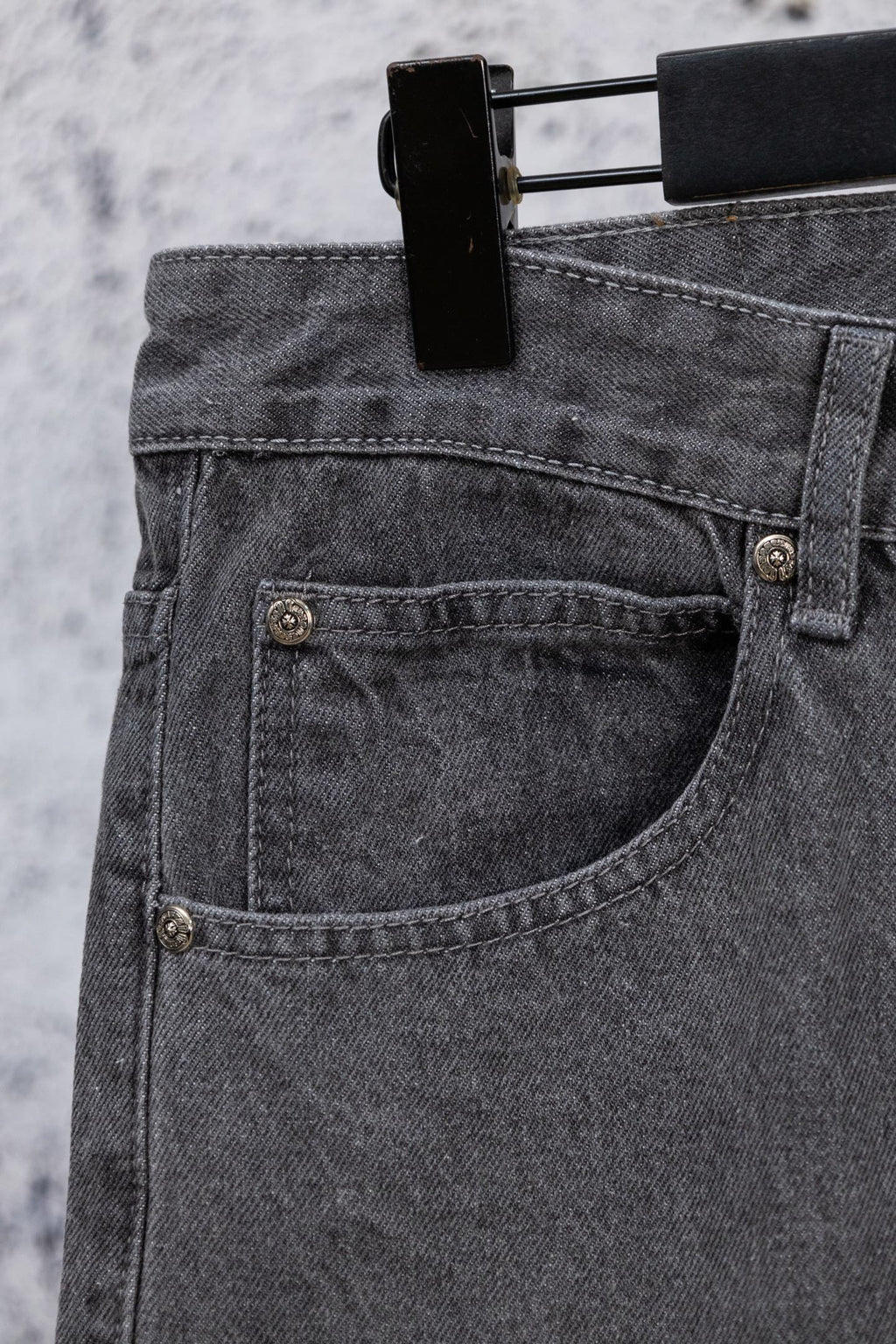 Gray denim pants close-up of buttoned front pocket and curved seam detail.