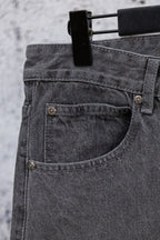 Gray denim pants close-up of buttoned front pocket and curved seam detail.