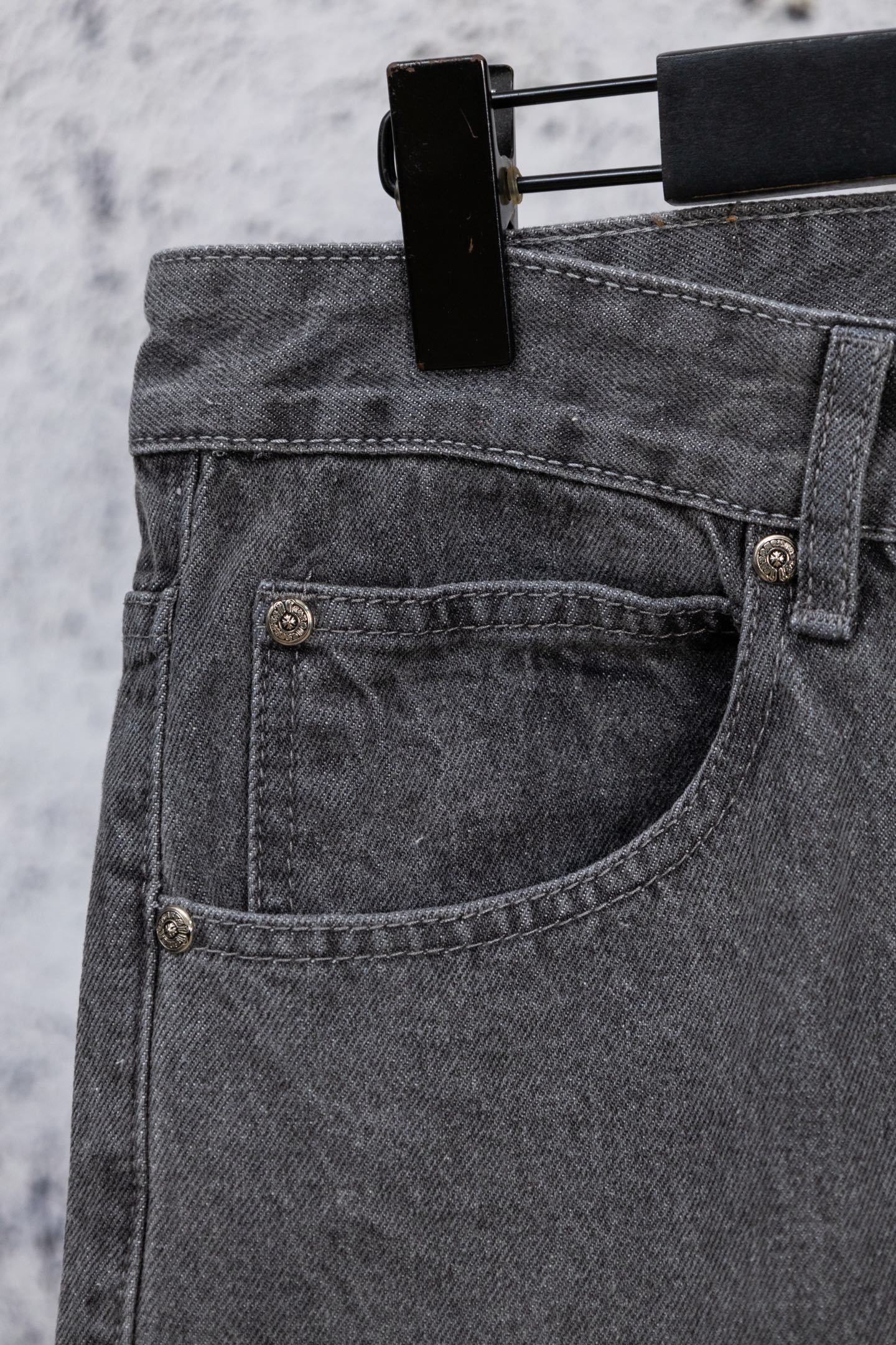 Gray denim pants close-up of buttoned front pocket and curved seam detail.