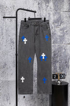 Gray denim pants with blue and white cross patches, front view on hanger.