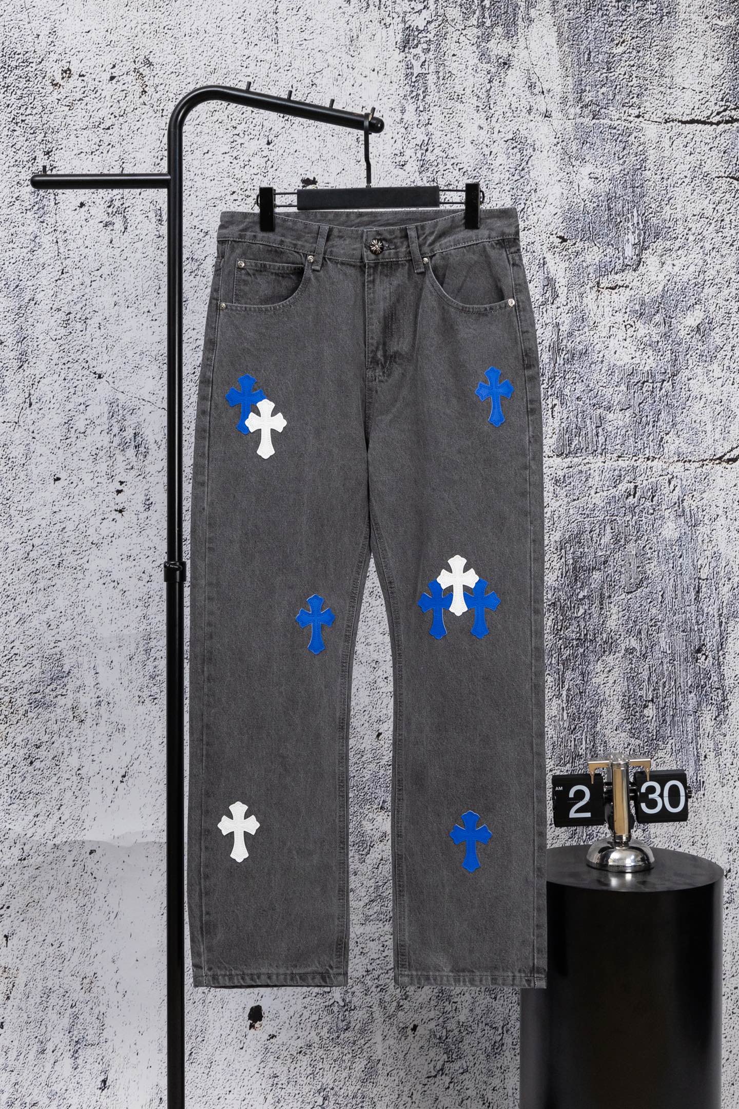 Gray denim pants with blue and white cross patches, front view on hanger.