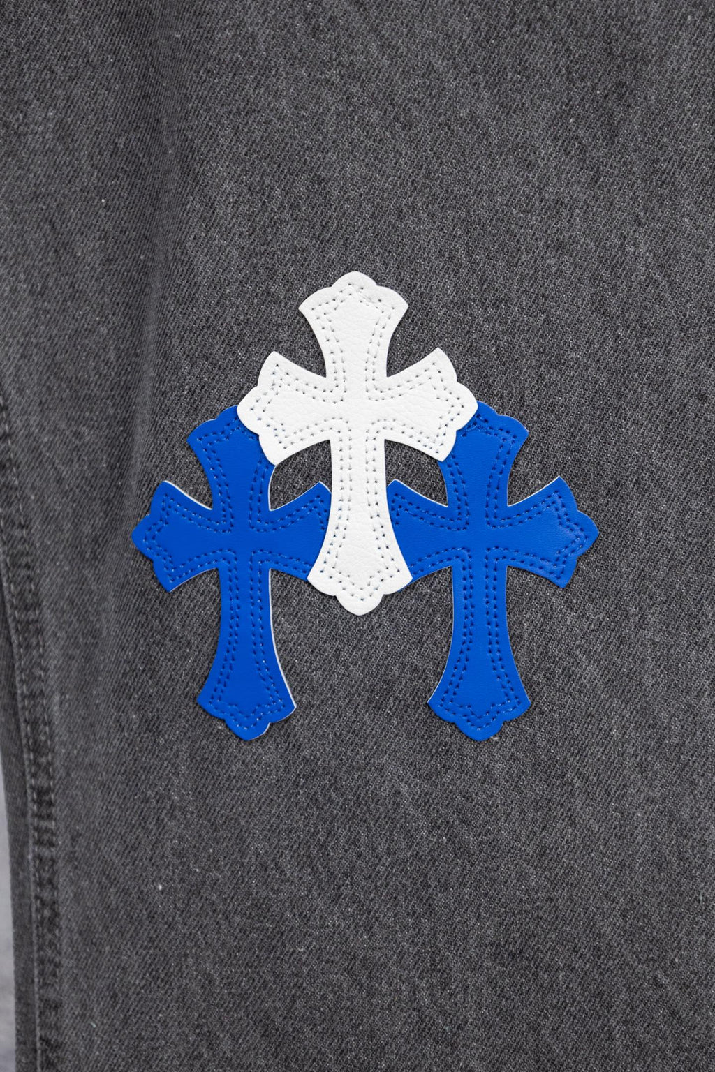 Chrome pants side close-up with blue and white cross applique on dark denim