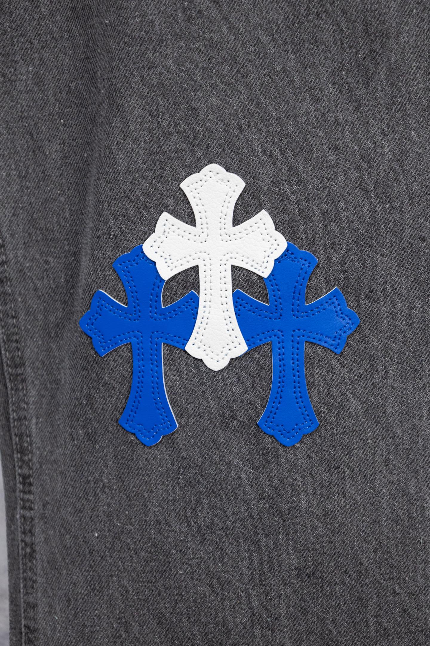Chrome pants side close-up with blue and white cross applique on dark denim