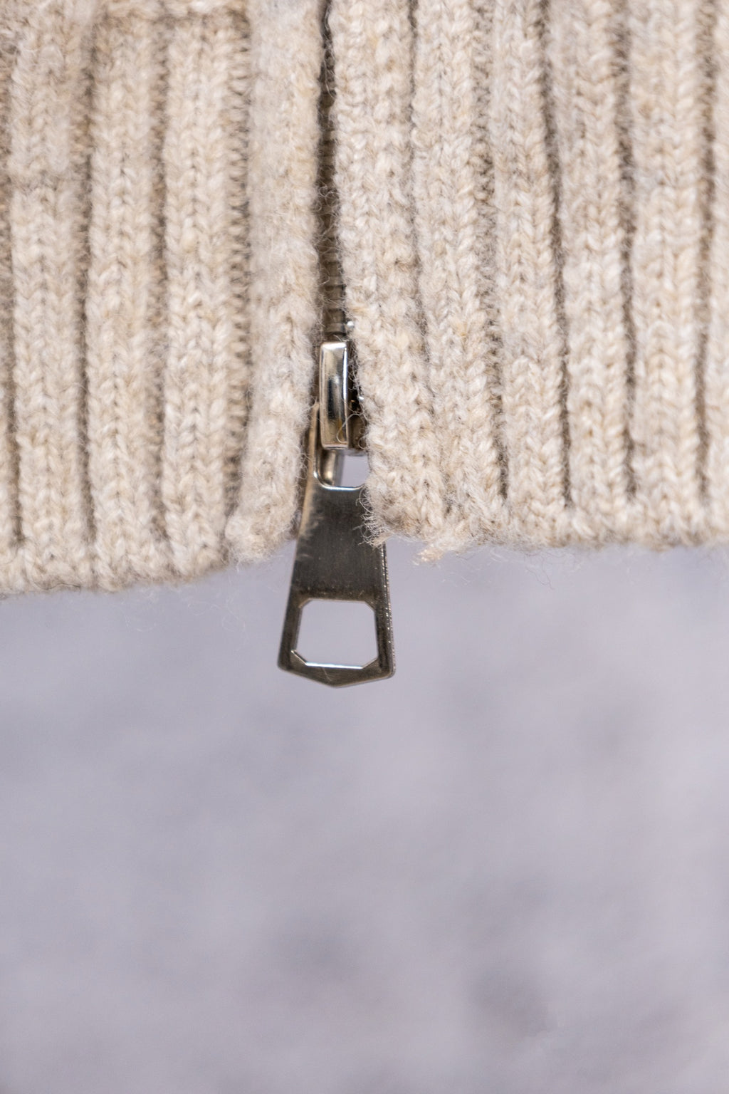 Cream ribbed sweater cuff with metal zipper tab close-up