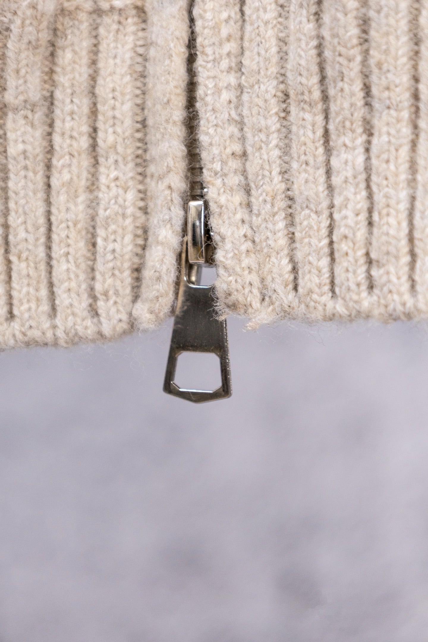 Cream ribbed sweater cuff with metal zipper tab close-up