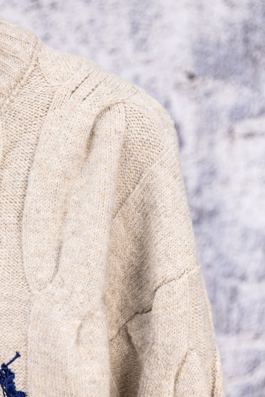 Cream knit sweater shoulder and sleeve with textured cable design