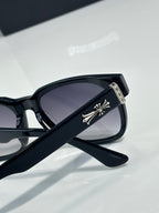 Black sunglasses with dark lenses and silver cross-like temple emblem