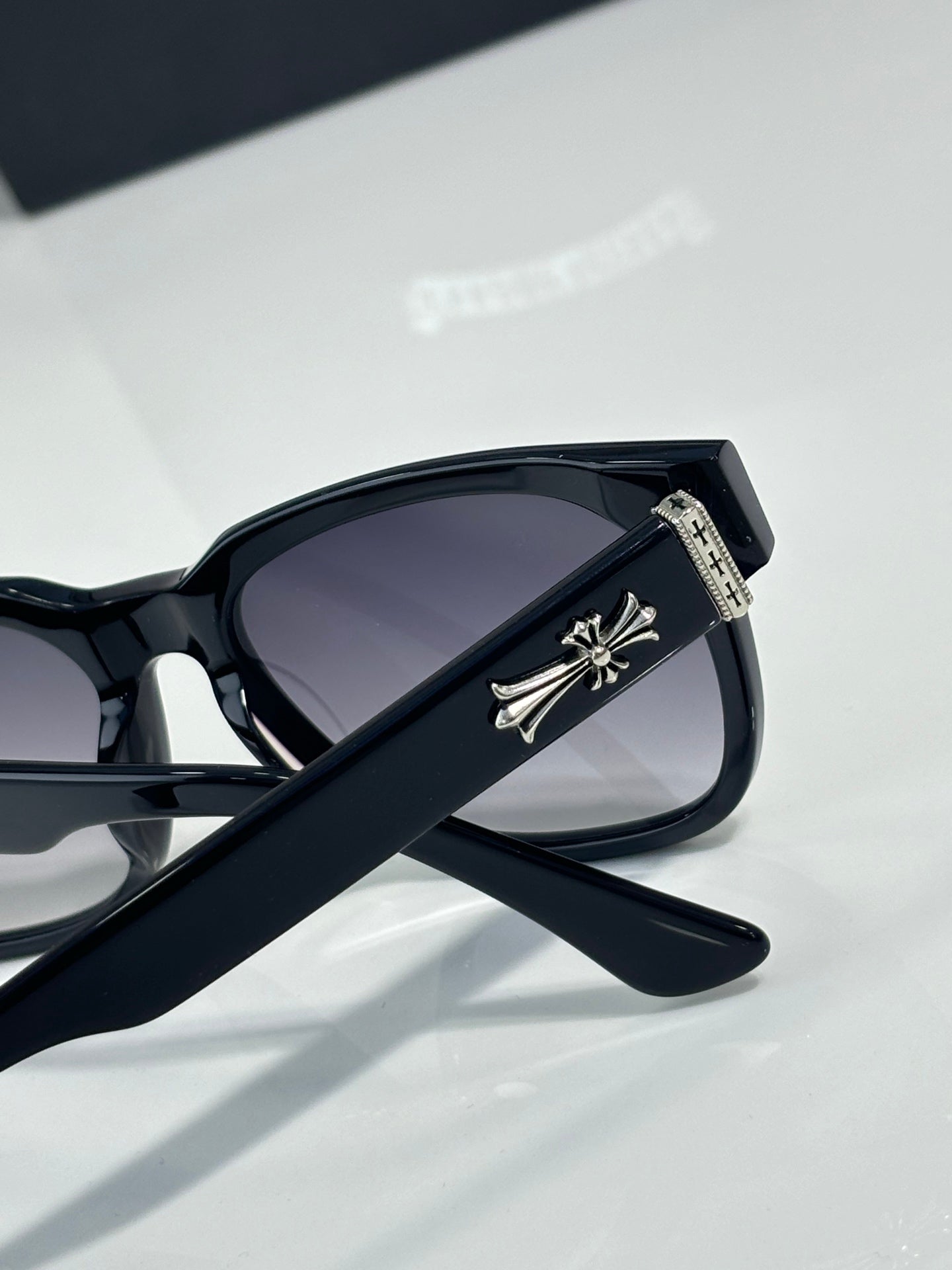Black sunglasses with dark lenses and silver cross-like temple emblem