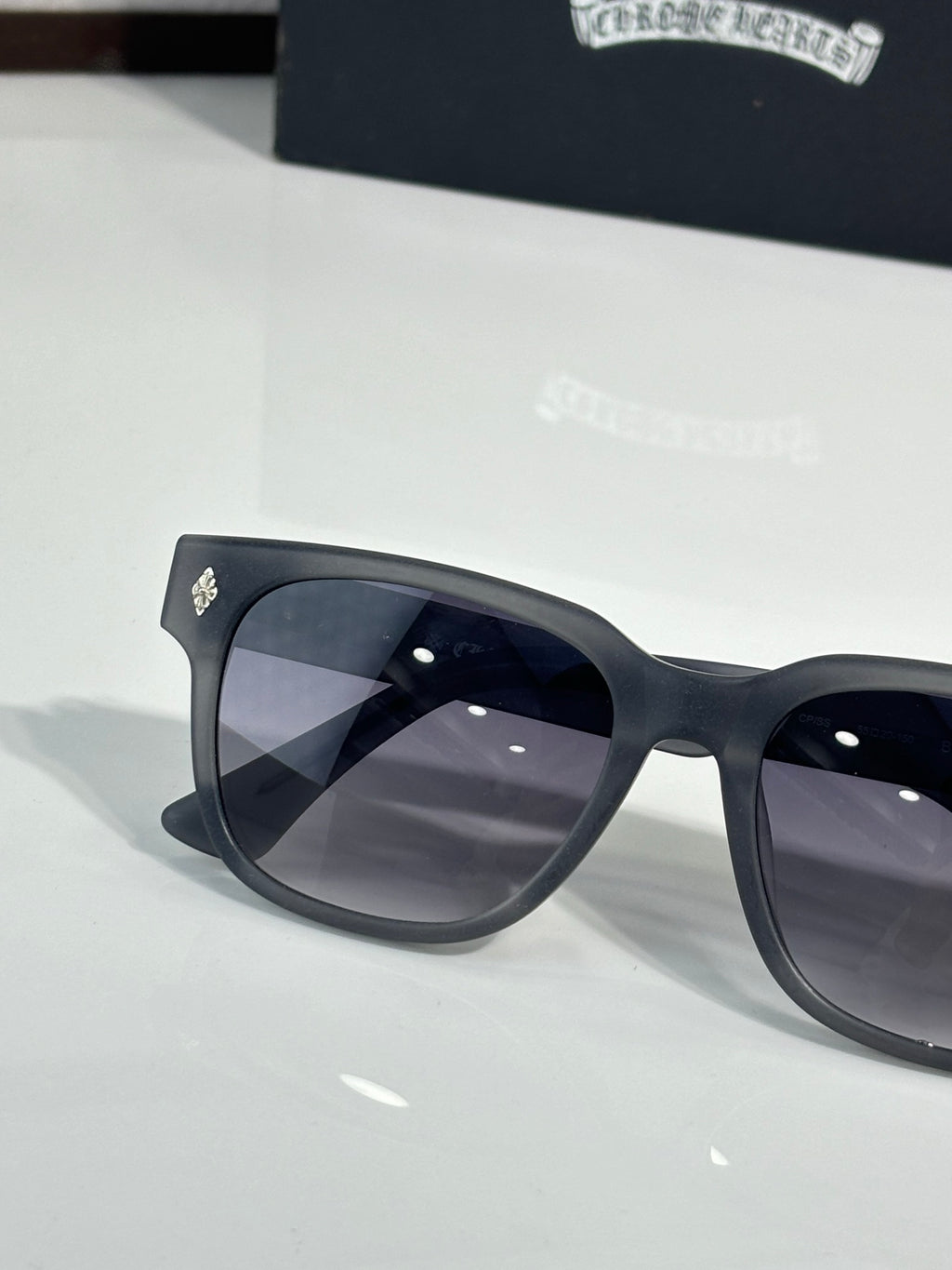 Black cat-eye sunglasses with dark lenses, close-up left frame