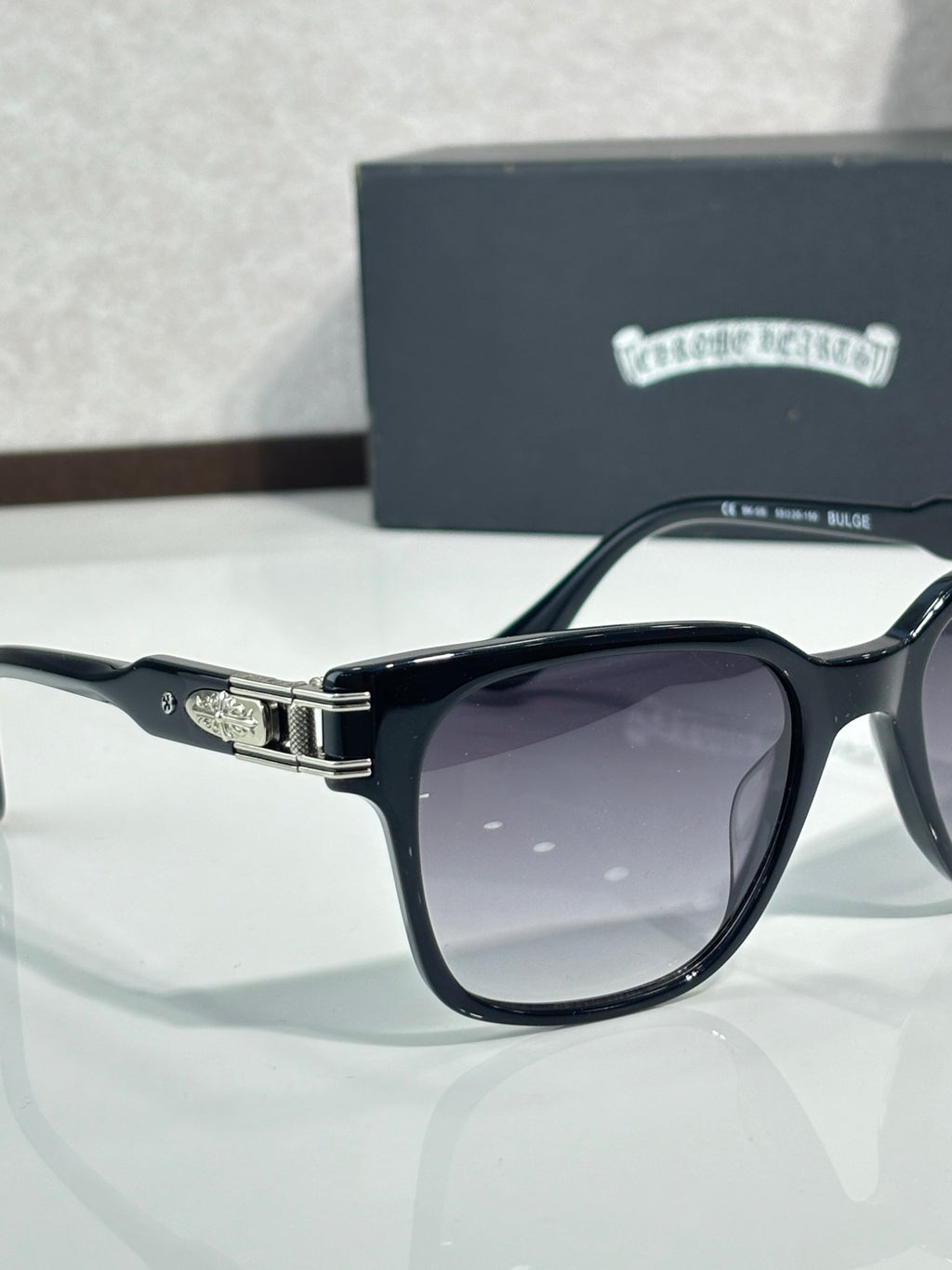 Black sunglasses with dark lenses, chrome-style hinge hardware, and engraved temple