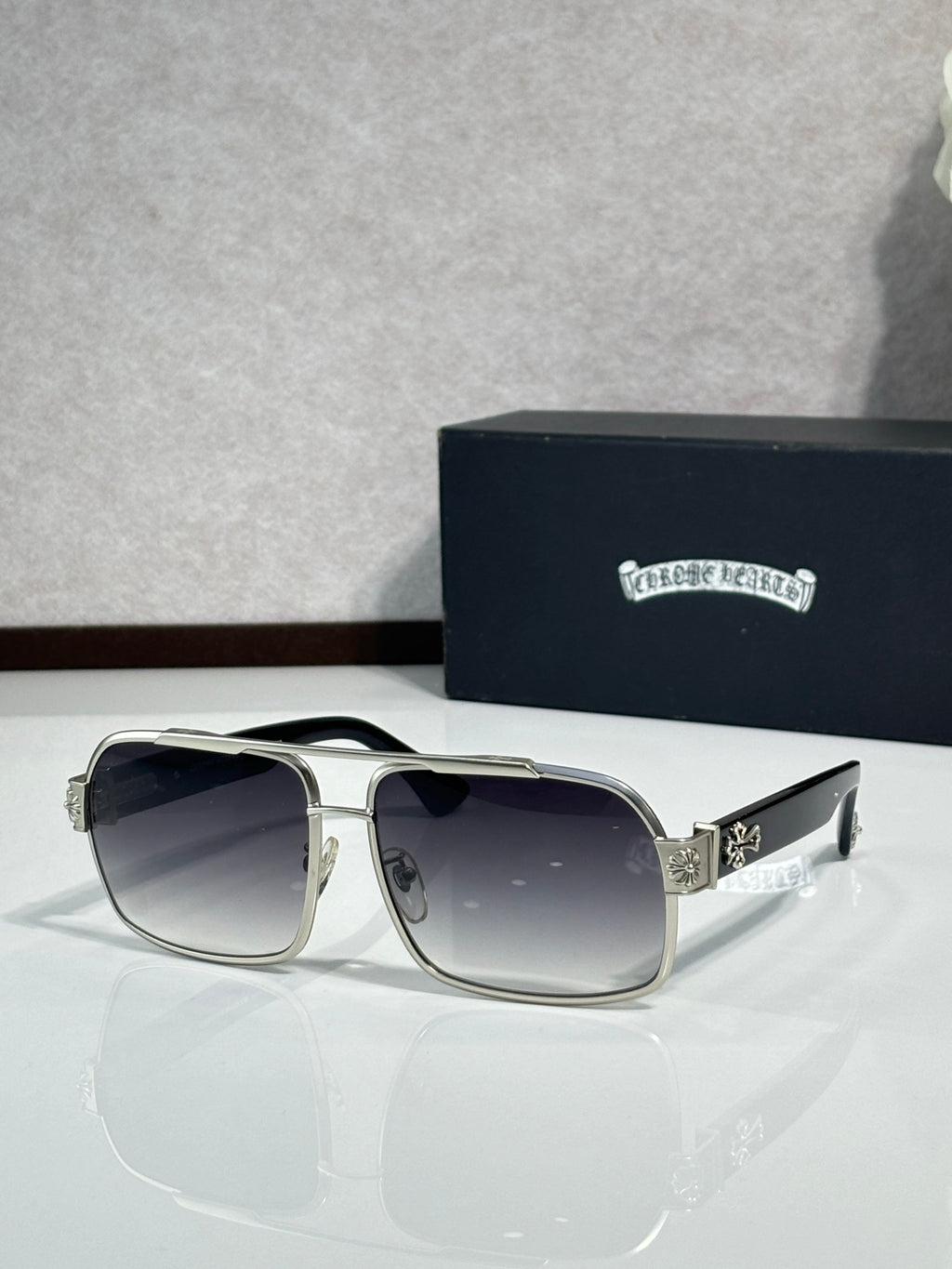 Silver square sunglasses with dark lenses and ornate side emblem