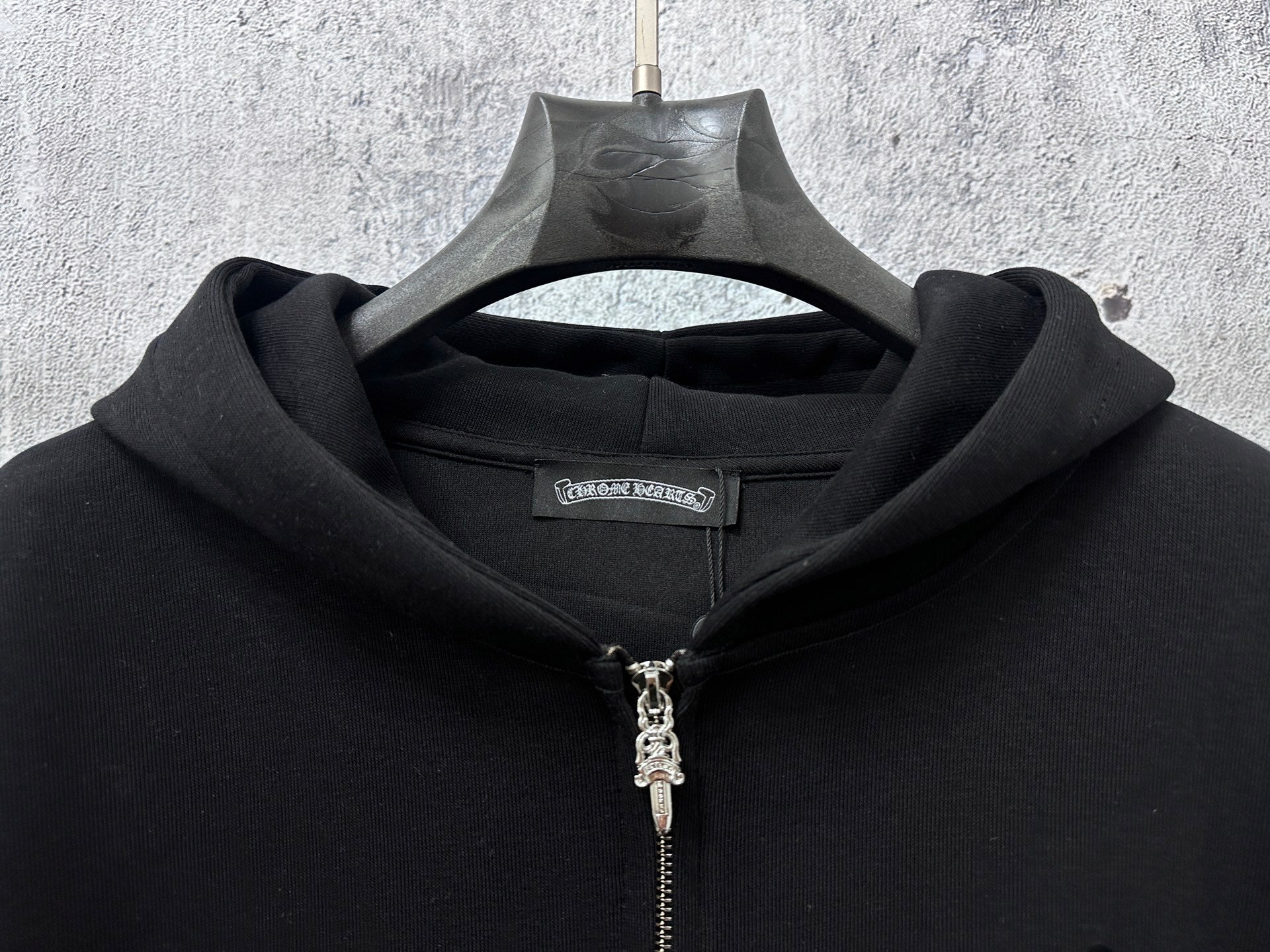 Black zip-up hoodie hood and silver front zipper with small neck logo tag