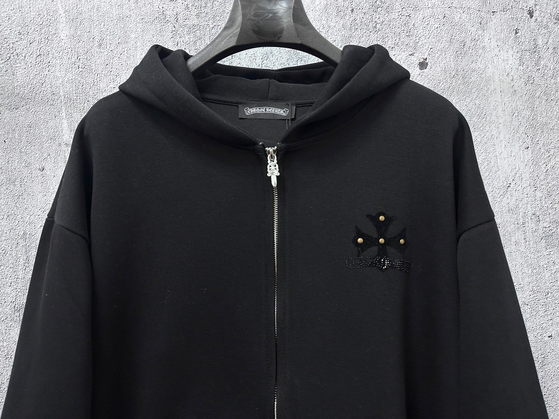 Black zip-up hoodie with rhinestone star-like chest emblem and silver zipper