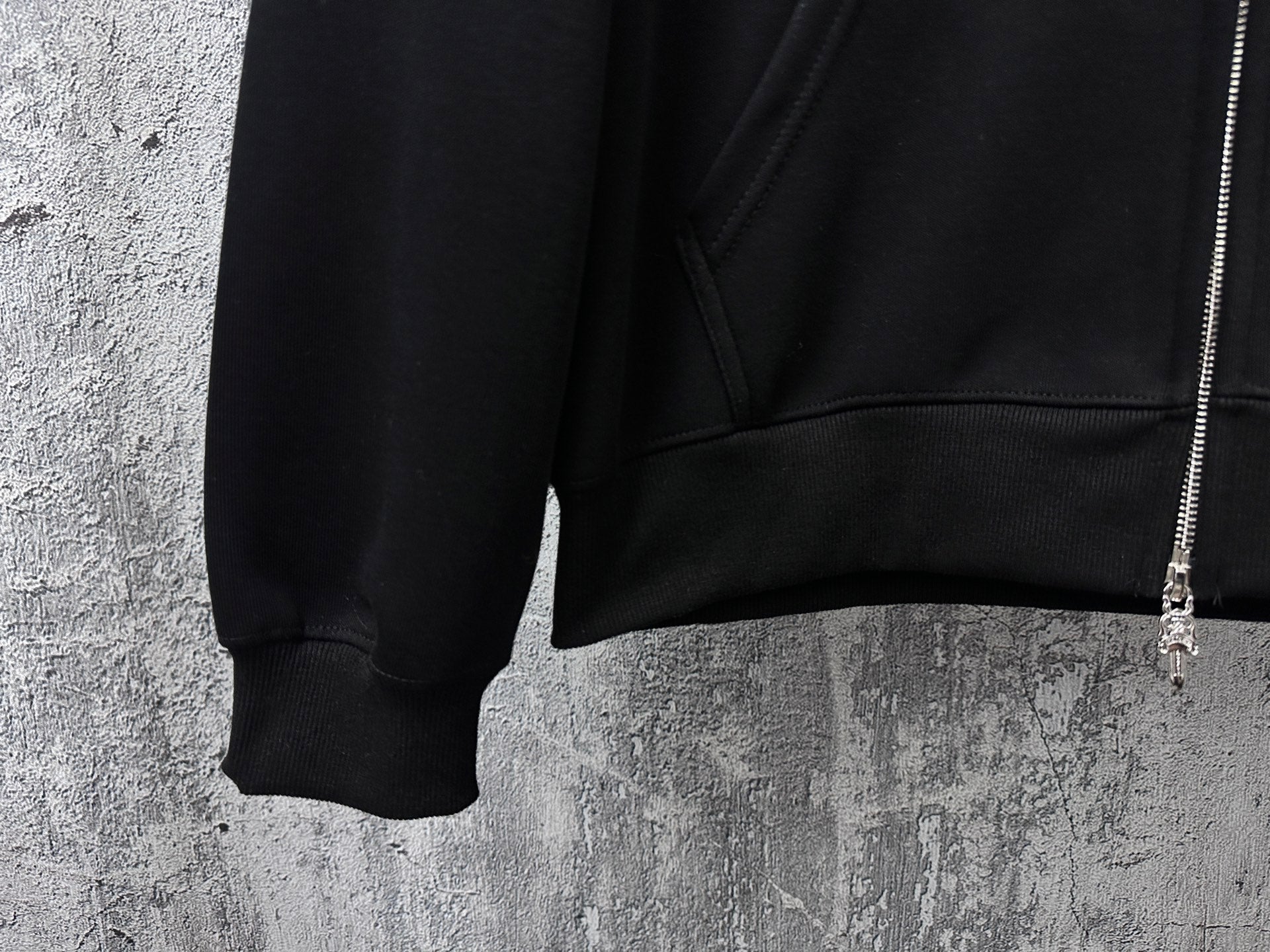 Black zip-up hoodie lower front pocket area and ribbed hem with zipper