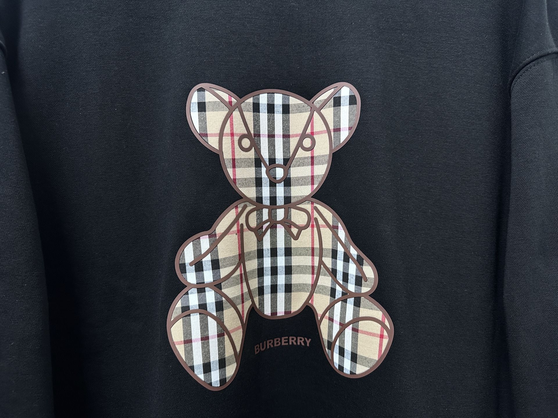 Black sweatshirt close-up of plaid teddy bear applique and Burberry logo