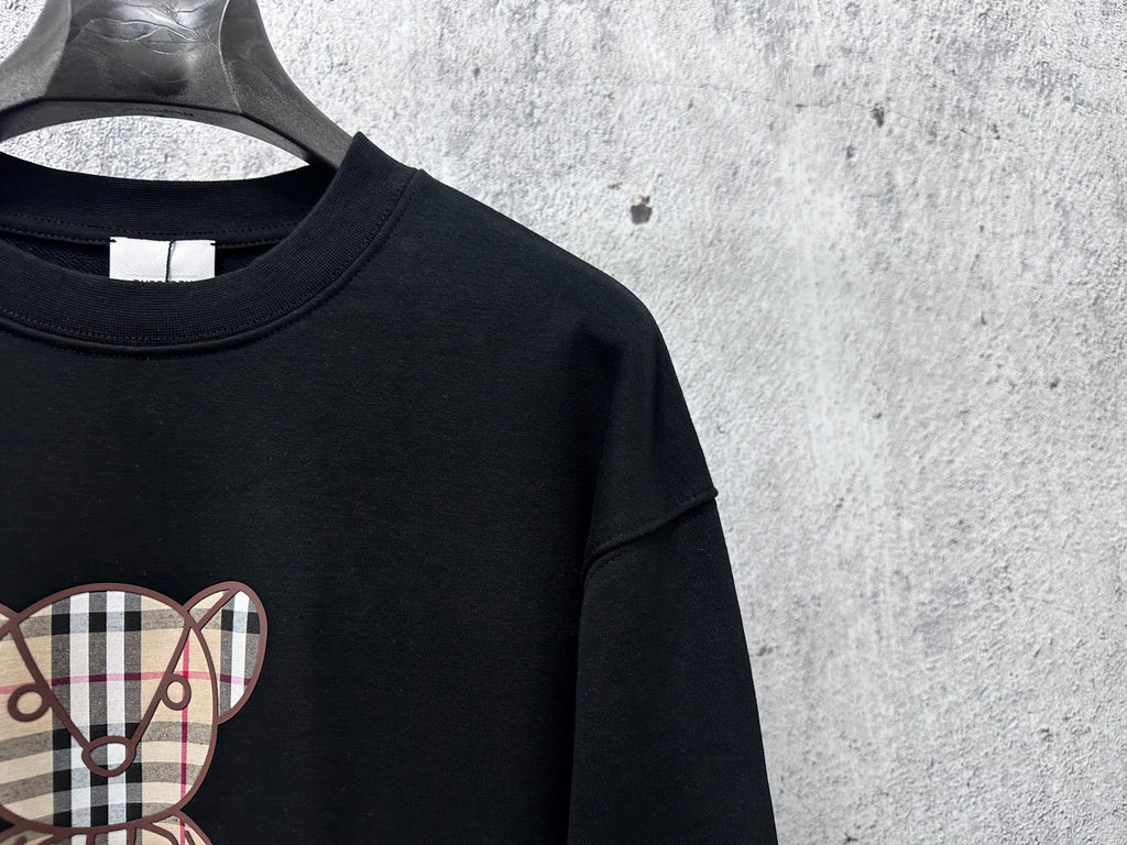 Black sweatshirt with partial plaid teddy bear graphic on chest