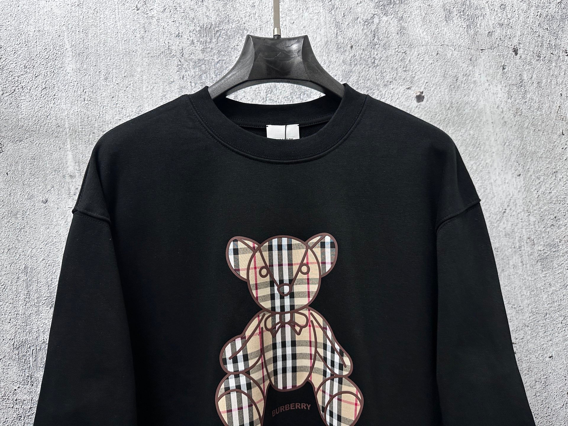 Black long-sleeve sweatshirt with full plaid teddy bear patch and bow