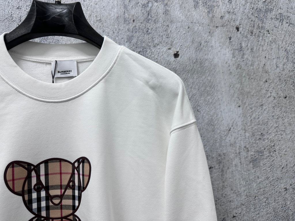 White sweatshirt with check-pattern teddy bear graphic, crewneck collar detail