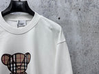 White sweatshirt with check-pattern teddy bear graphic, crewneck collar detail