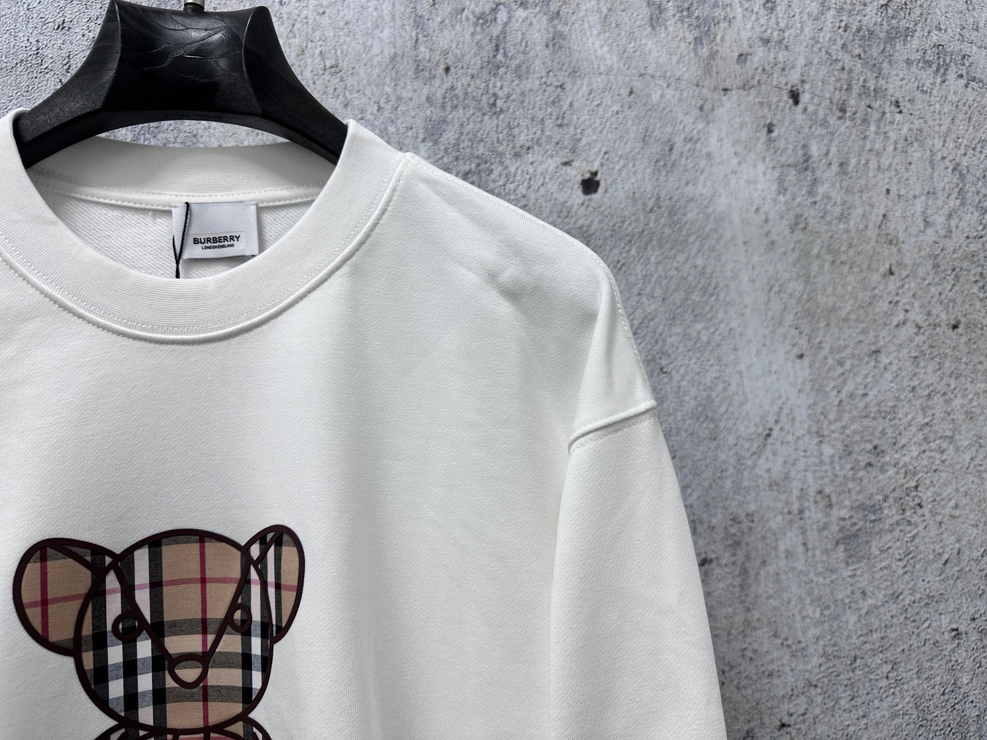 White sweatshirt with check-pattern teddy bear graphic, crewneck collar detail