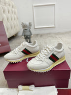 Two white Gucci unisex sneakers with lace-up front, green/red stripe, and yellow sole