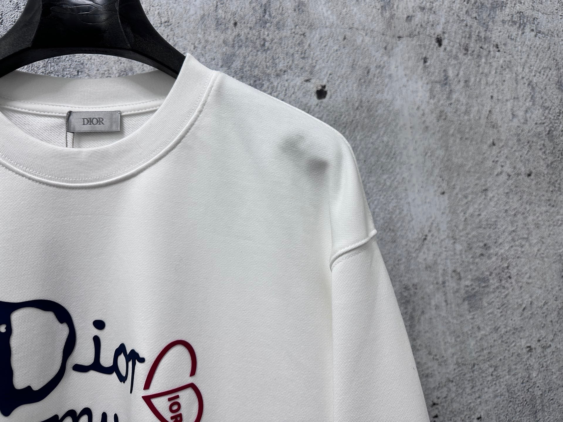 White sweatshirt neckline close-up with Dior tag and partial logo graphic