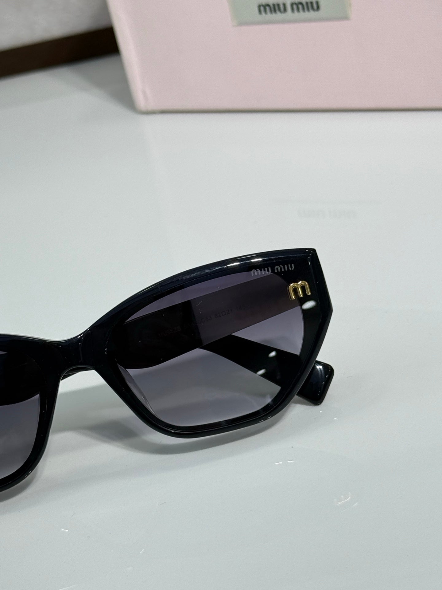 Black sunglasses close-up with dark lenses beside pink logo case