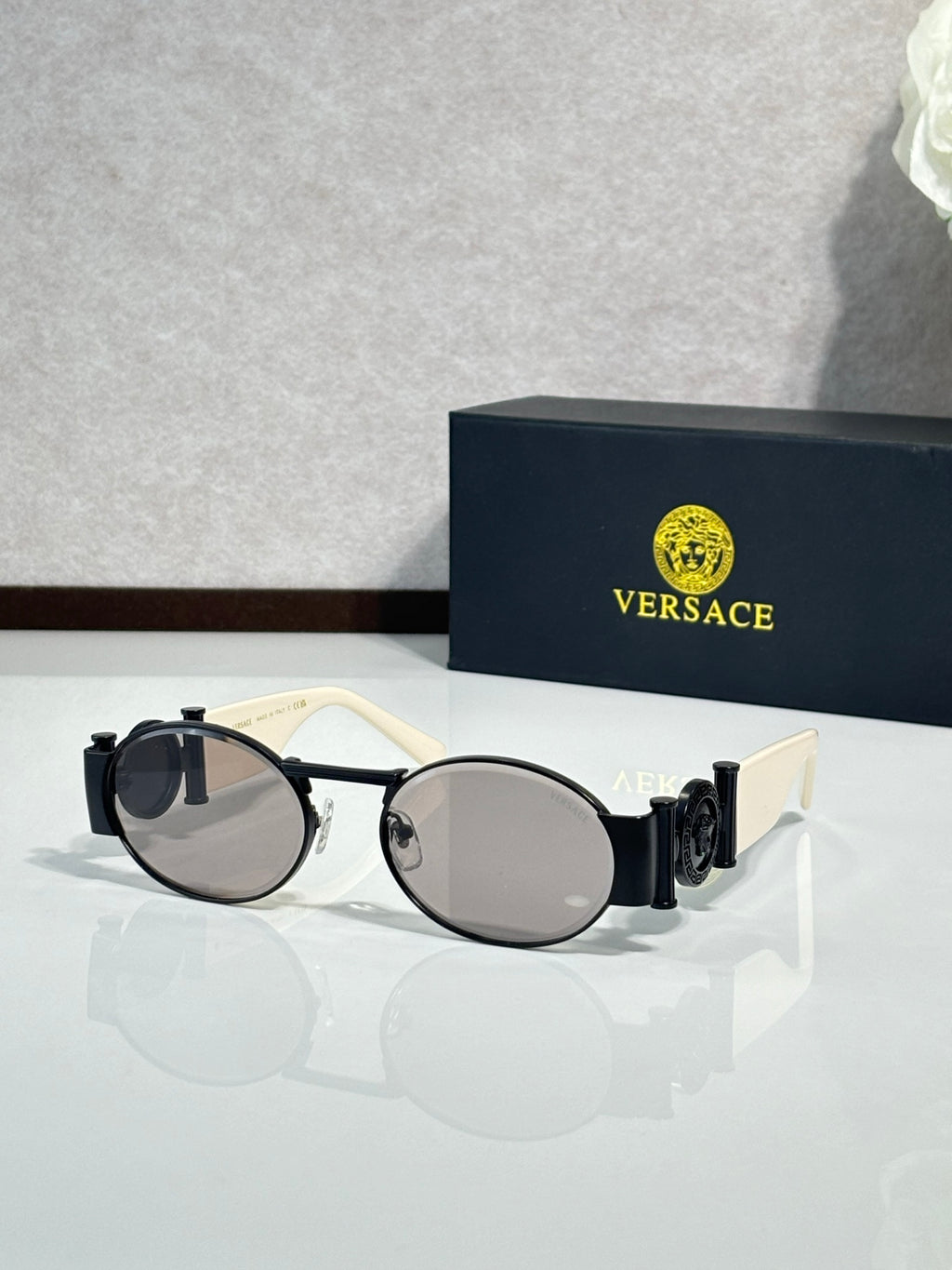 Versace sunglasses with round lenses, white frame with dark arms and dark lenses.