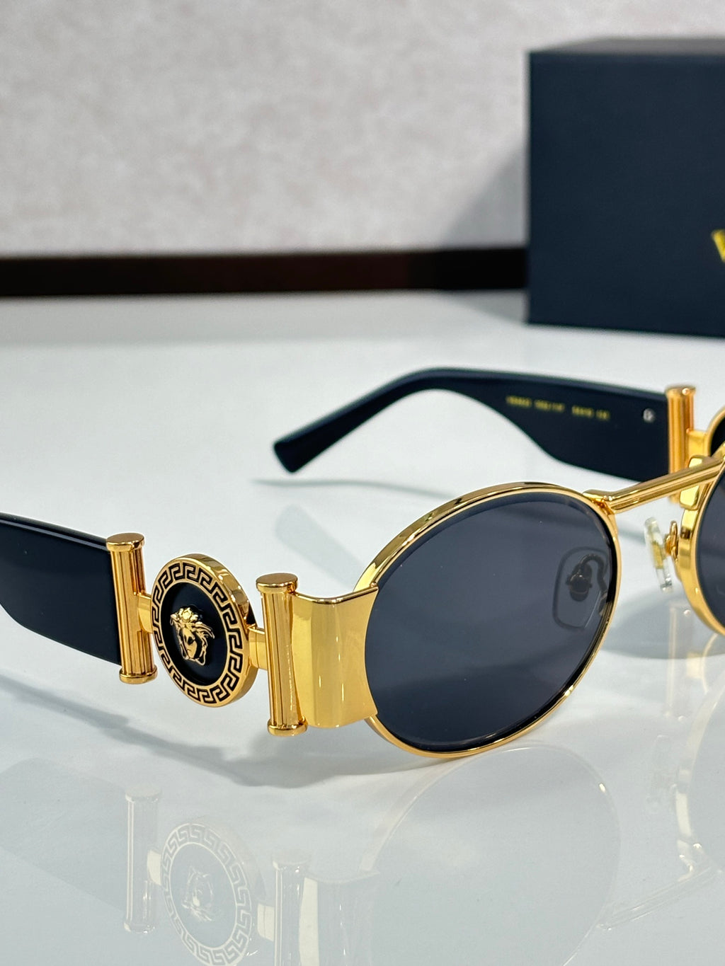 Versace sunglasses with round lenses, gold frame and dark lenses, side detail visible.