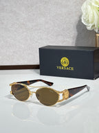 Gold round sunglasses with dark lenses and brown-tinted accents at the temples, on a reflective surface.