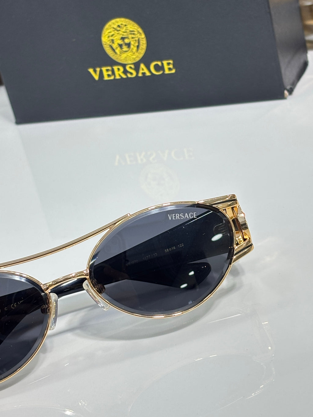 Close-up of gold oval sunglasses with dark lenses and a temple logo medallion detail.