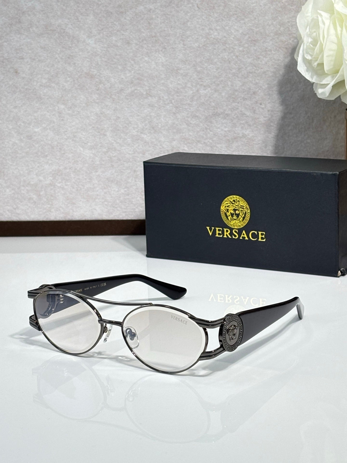 Metal eyeglasses with clear lenses and a dark temple medallion detail, oval profile.