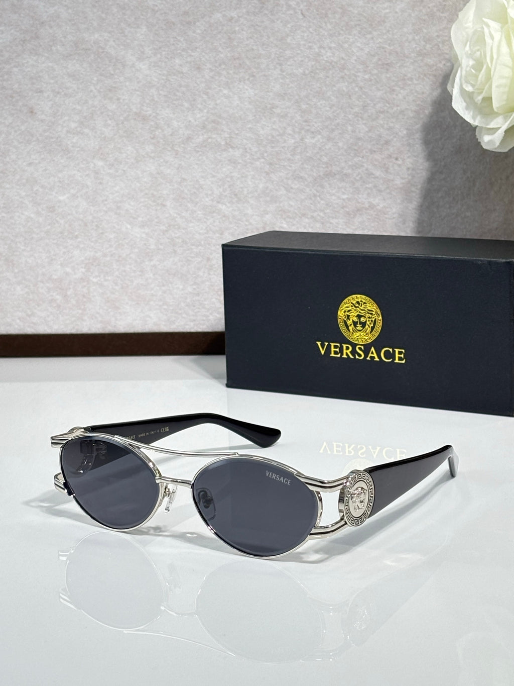 Silver-gray framed sunglasses with dark lenses and a circular medallion on the temple.