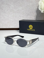 Silver-gray framed sunglasses with dark lenses and a circular medallion on the temple.