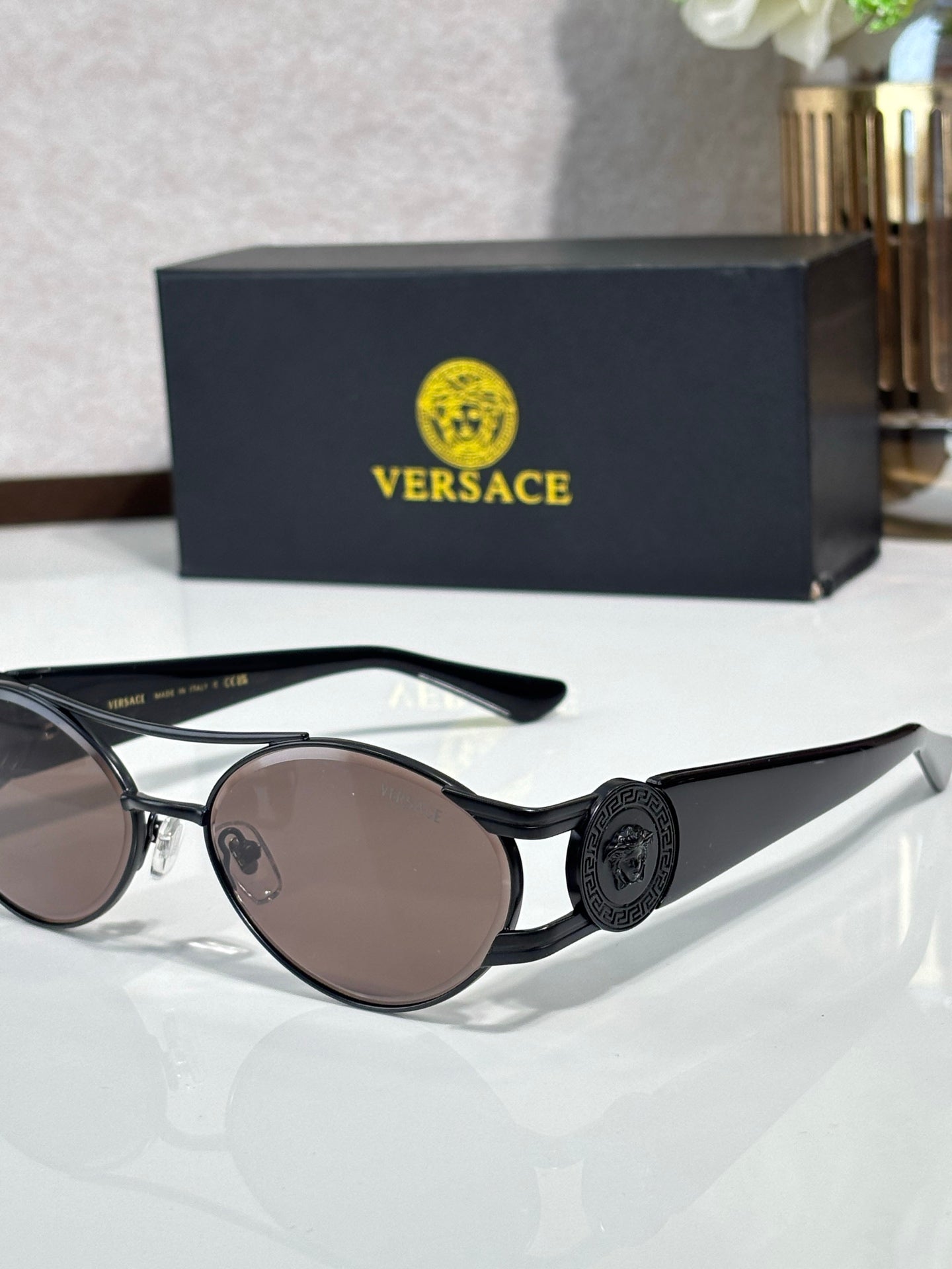 Black round sunglasses with dark lenses and a circular medallion on the temple, mirrored finish.