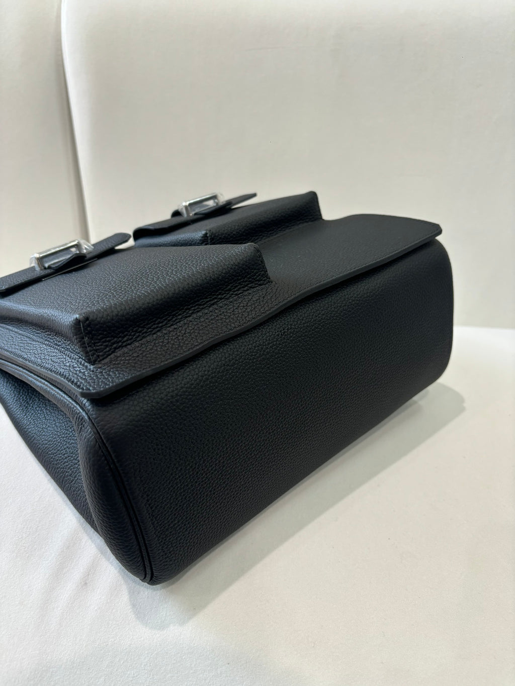 Hermes pebbled leather flap bag side view with silver top hardware and strap loops