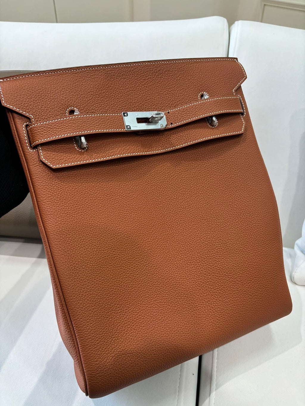 Hermes bag front view in tan brown leather with stitched flap, silver clasp, and side straps.