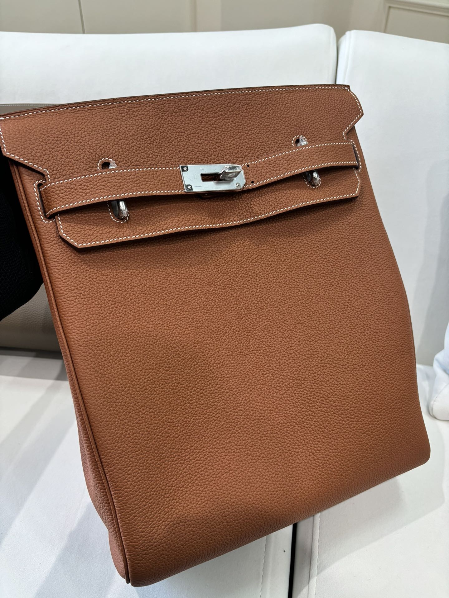 Hermes bag front view in tan brown leather with stitched flap, silver clasp, and side straps.