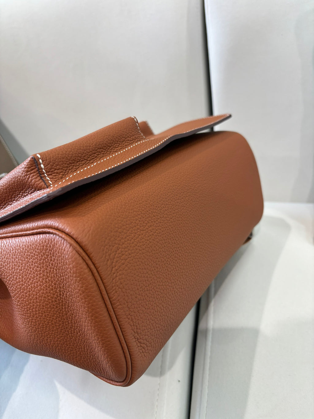 Hermes bag side profile in tan brown leather, rounded base and top flap with silver clasp.