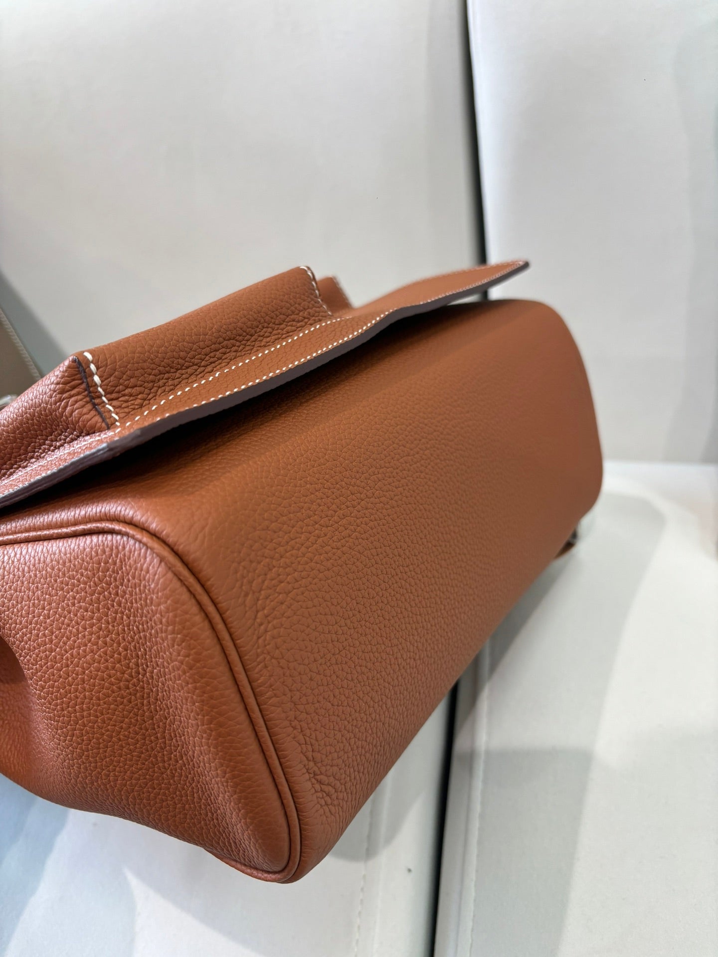 Hermes bag side profile in tan brown leather, rounded base and top flap with silver clasp.