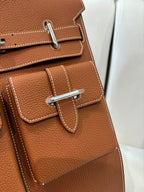 Hermes bag close-up: tan brown leather pocket flap with stitched trim and silver latch.