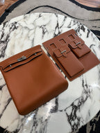 Pair of Hermes bags in tan brown leather with front flap, silver buckles, and stitched edges.