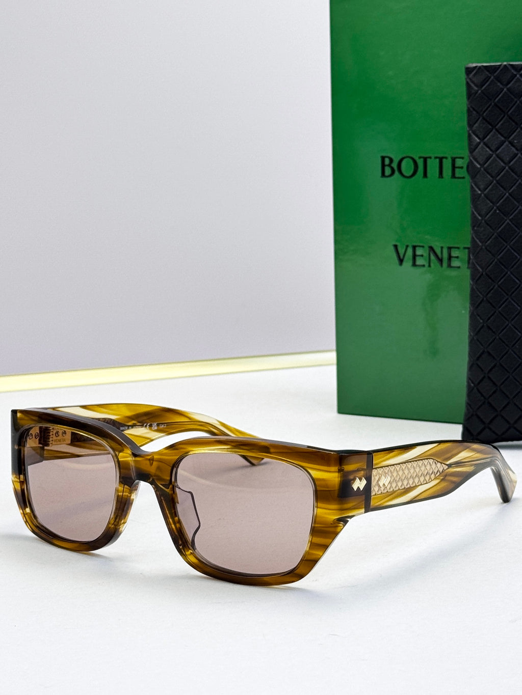 Bottega Veneta sunglasses with amber tortoise frames, gray lenses, and gold patterned temples