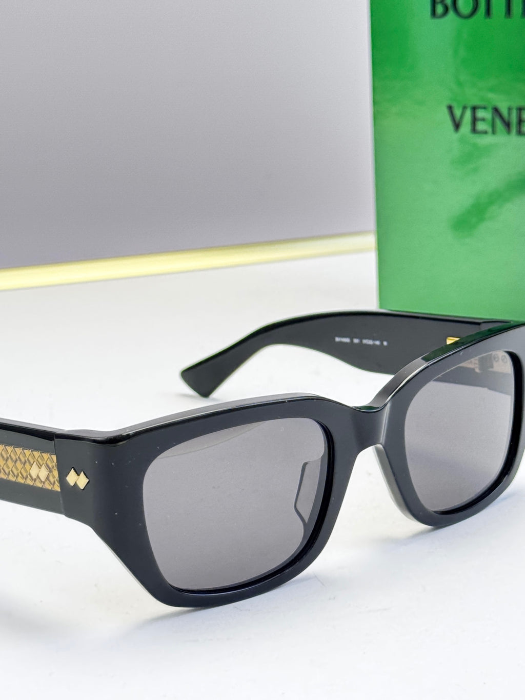 Bottega Veneta sunglasses with black frames and dark gray lenses, gold patterned temple detail