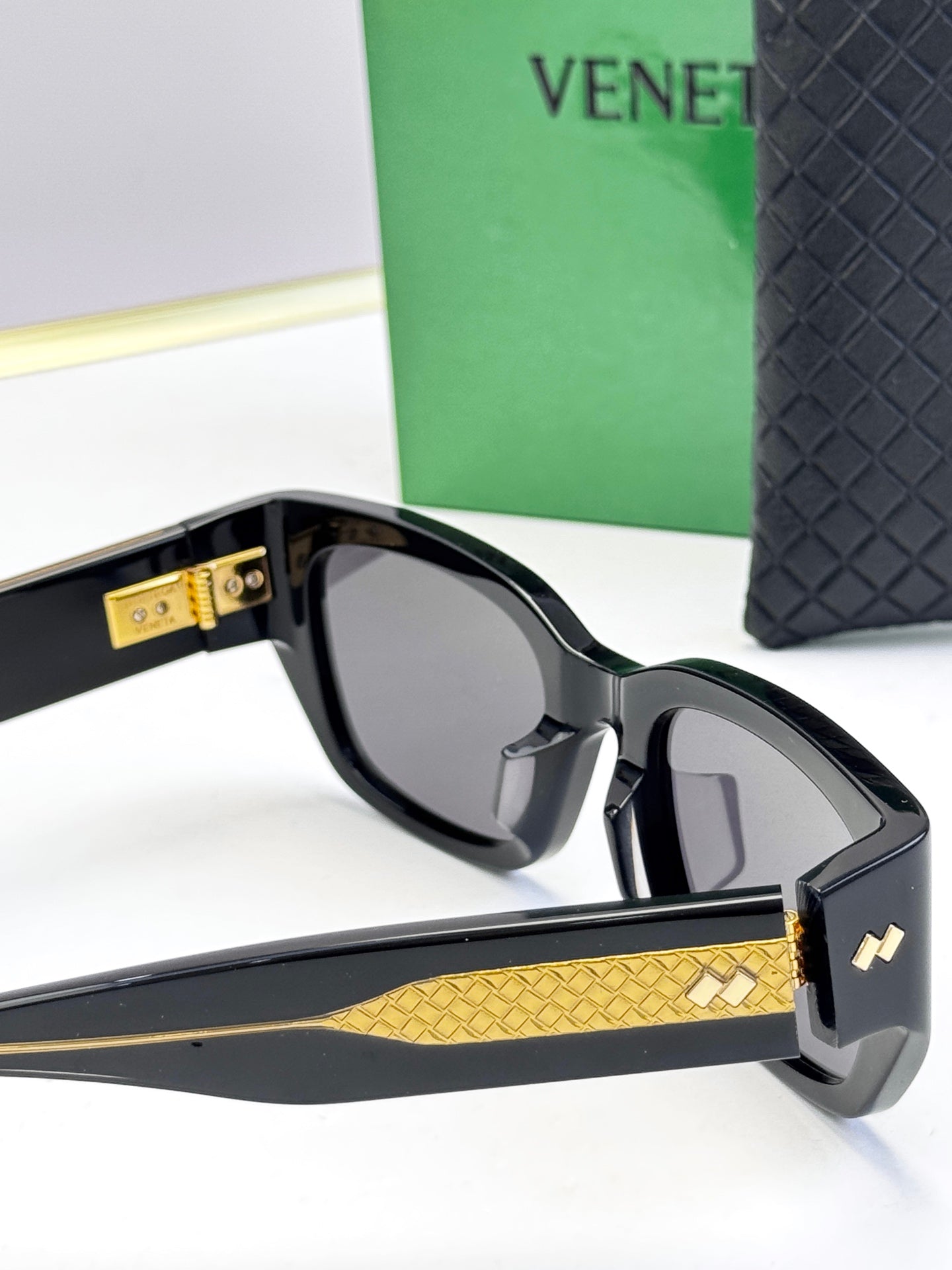 Bottega Veneta sunglasses with black frames, gold patterned temple, and gold logo accent