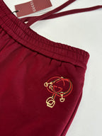 Burgundy pants with elastic waistband and gold-tone crest embroidery on thigh