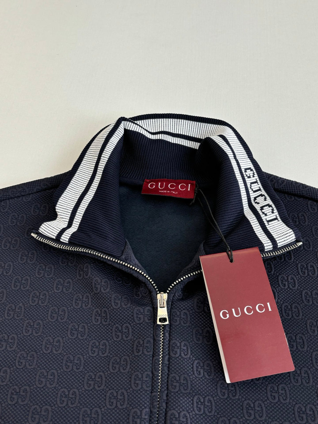 Navy Gucci track jacket collar with white striped trim and logo tag