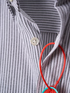 Striped shirt placket with gold button and red loop keychain tag