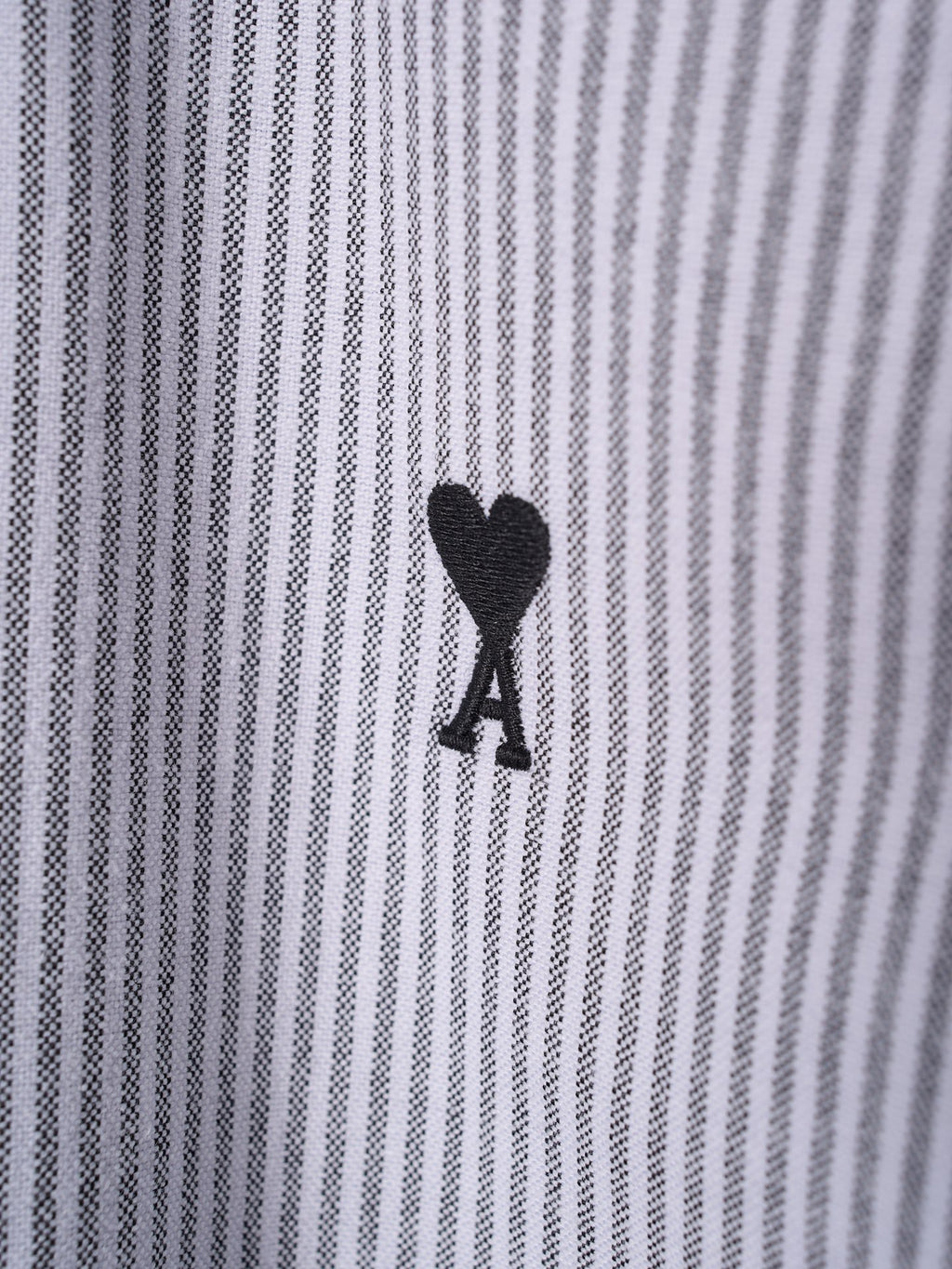 Small black A emblem on light blue and white striped shirt