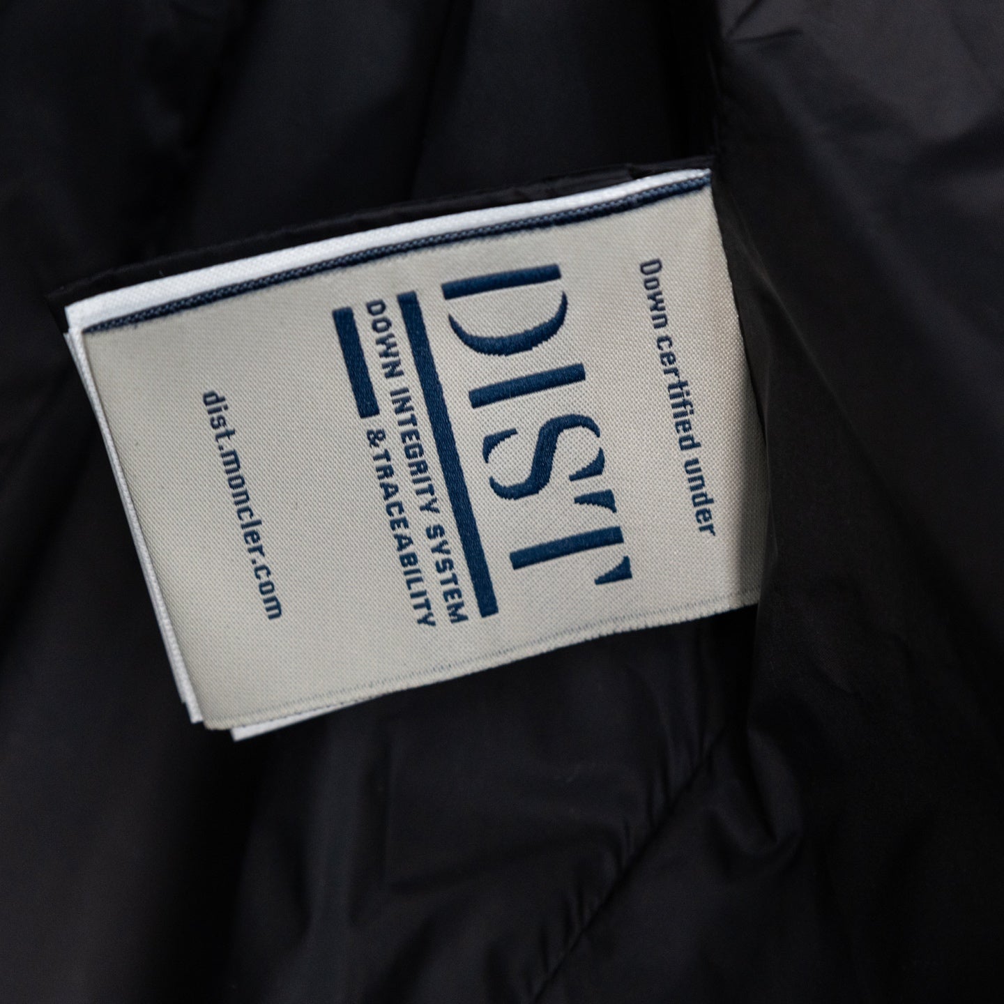 Long puffer jacket inner label with blue text and 'Down Certified' logo.